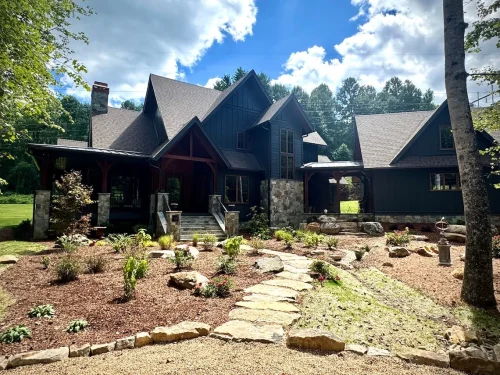 Closer view of mountain home with stone steps leading to covered porch and landscaped garden.