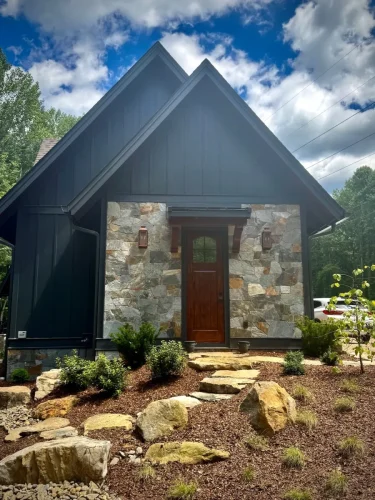 Side entrance of stone and wood mountain home with peaked rooflines, landscaped path, and wood door.