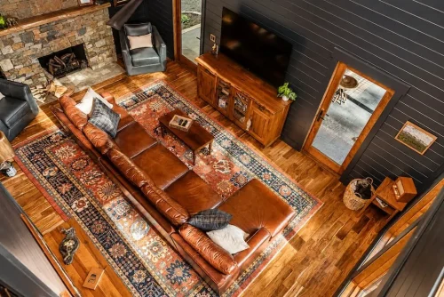 Overhead view of a living room with leather sectional, stone fireplace, hardwood floors, and patterned area rug.