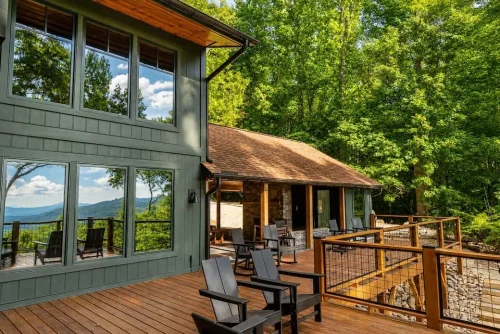 Spacious wood deck with outdoor seating, cable railing, and mountain views through the surrounding trees.