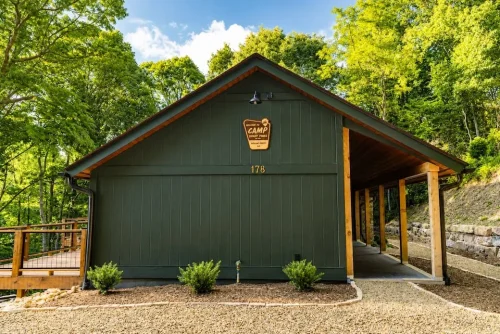 Side exterior of a dark green mountain home with a covered walkway and surrounding wooded landscape.