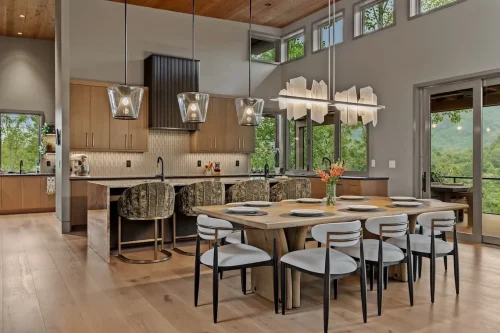 Open kitchen and dining area with warm wood cabinetry, statement lighting, and large windows overlooking the mountains.