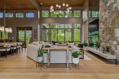Open great room with soaring windows, a stone fireplace, wood ceiling, and mountain views.