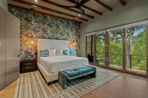 Bedroom with exposed wood ceiling beams, a textured accent wall, and sliding doors opening to a mountain-view deck.