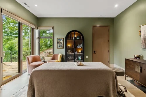 Wellness room with soft green walls, a treatment table, and direct access to an outdoor patio.