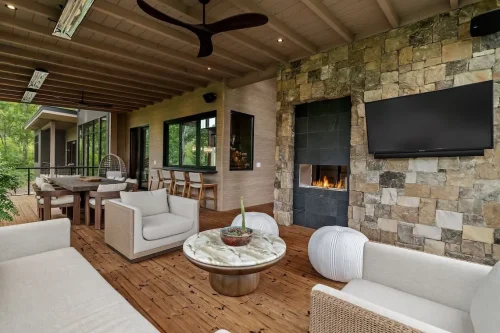 Covered outdoor living and dining area with a stone fireplace, television, wood decking, and built-in bar seating.