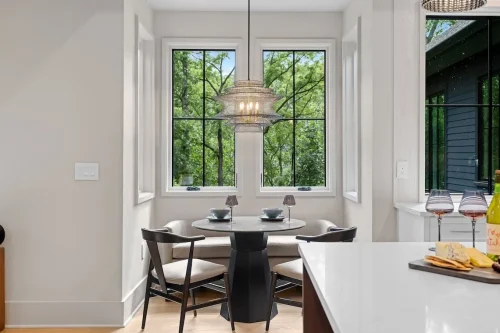 Bright breakfast nook with large windows overlooking the woods, built-in seating, and a round dining table.