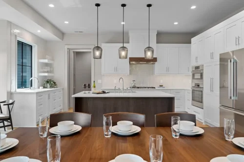 Modern kitchen with white cabinetry, a large island, dark wood accents, stainless steel appliances, and pendant lighting
