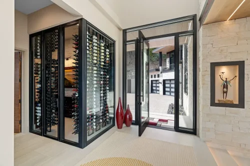 Glass-enclosed wine room beside a black-framed entry door, with stone walls and decorative accents.