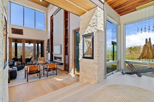Open living space with stone accents, a fireplace, tall windows, wood flooring, and an adjacent display area with mountain views.