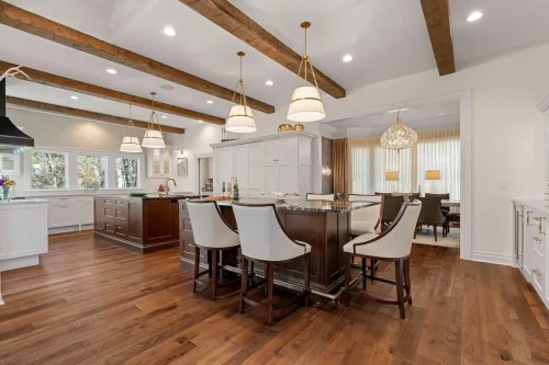 Open kitchen featuring two dark wood islands, white cabinetry, exposed ceiling beams, pendant lighting, and an adjoining dining room.