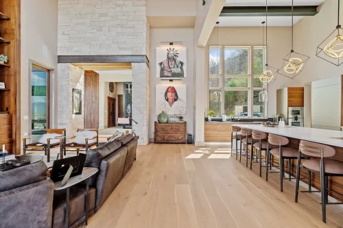 Open-concept living and kitchen area with tall ceilings, large windows, a long island, wood cabinetry, and stone architectural details.