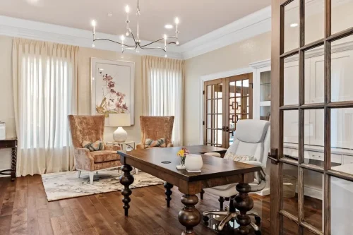 Home office featuring a dark wood desk, upholstered seating, hardwood floors, large windows, and glass French doors.