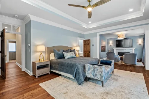 Spacious primary bedroom with blue walls, hardwood floors, a tray ceiling, upholstered bed, and an adjoining sitting area with a fireplace.