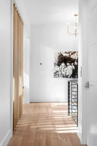Bright hallway with white walls, wood slat divider, and natural light, showcasing a large black-and-white horse portrait as focal art.