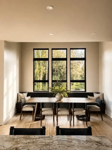 Dining area with a wood table, built-in bench seating, black-framed windows, and warm wood flooring.