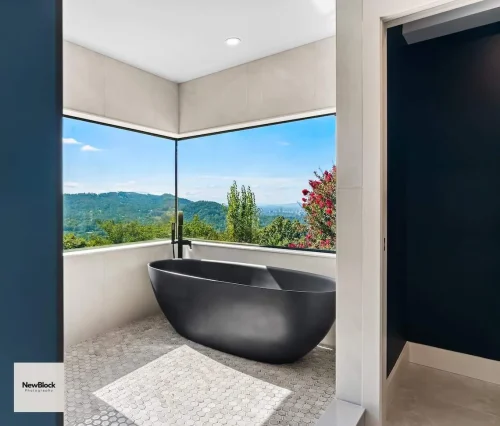 Freestanding black bathtub with mountain views through corner windows.
