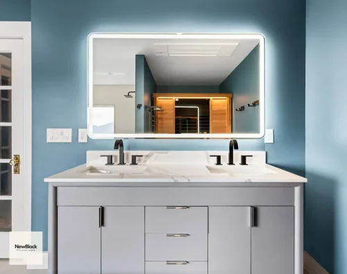 Close-up of vanity and lighted mirror with sauna reflected in glass.