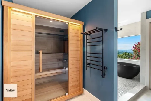 Wooden sauna with glass door and black towel warmer beside it.