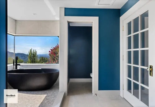 Modern bathroom with black tub, blue walls, and mountain view.