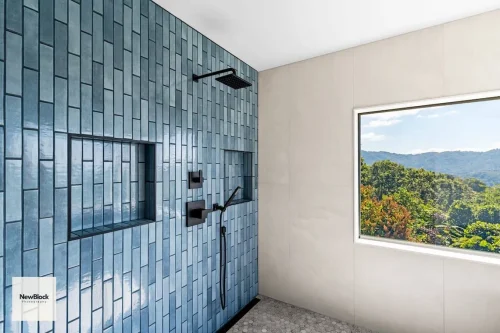 Shower with blue tile wall and window overlooking mountains.