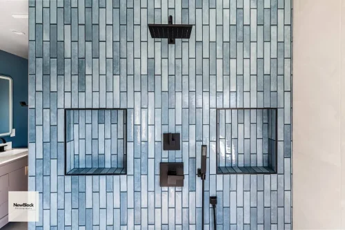 Close-up of blue tiled shower with black fixtures and niches.