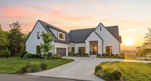 White contemporary home at sunset with steep gabled rooflines, dark trim, landscaped grounds, and mountain views.