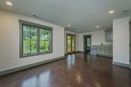 Basement living space with polished concrete floors, large window, French doors, and a kitchenette with gray cabinets.