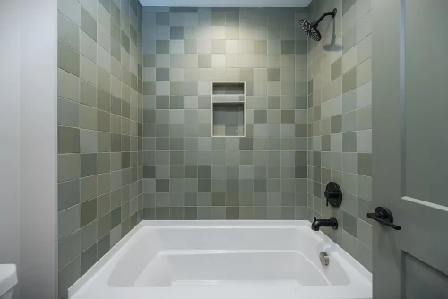 Bathroom with green square-tile shower surround, built-in niche, and black fixtures.