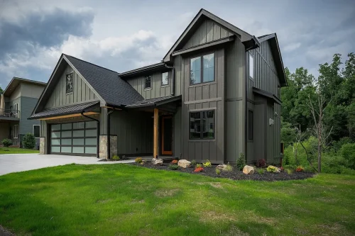 Exterior front view of modern craftsman home with dark green siding, stone accents, and landscaped front yard.