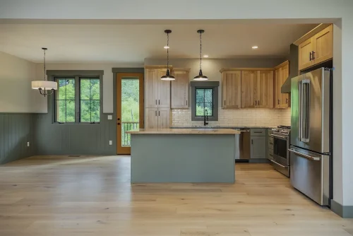 Kitchen and dining area with island, pendant lights, and wood cabinetry next to large windows and door to deck.