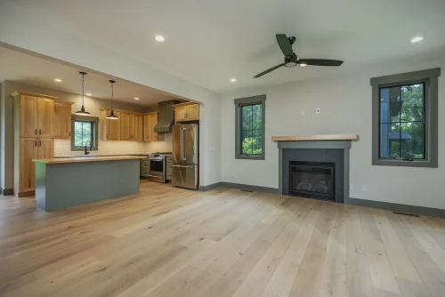 Open-concept living area with fireplace, hardwood floors, and view into kitchen with natural wood cabinets.