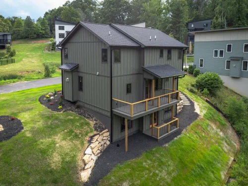 Rear exterior of two-story home with board-and-batten siding, two balconies, and terraced landscaping on hillside.