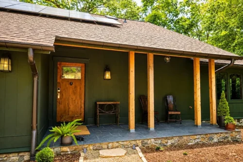 Covered front porch with dark green siding, natural wood posts, stone foundation, and wood entry door.