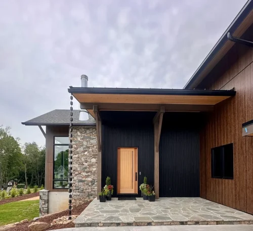 Covered front entry featuring wood siding, stone accents, black vertical siding, and a natural wood door.