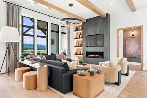 Living room with exposed wood ceiling beams, large black-framed windows, a dark fireplace surround, and mountain views.