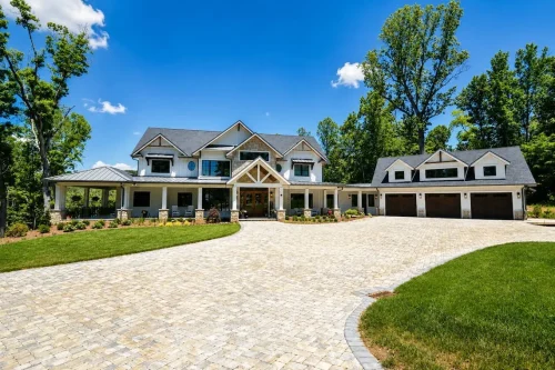 Wide front view of a large craftsman-style home with covered porches, multiple gables, stone details, and an attached three-car garage.