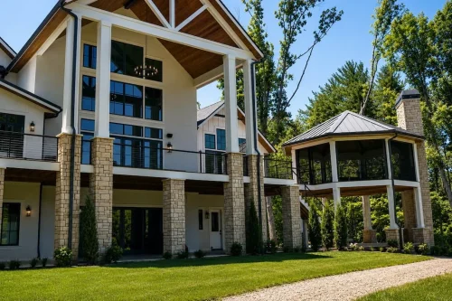Rear view of a large craftsman-style home with tall windows, stone columns, expansive decks, and a covered outdoor pavilion.
