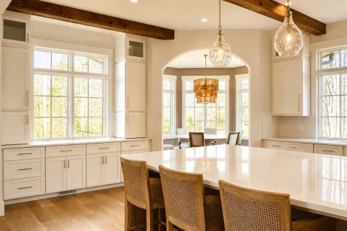 Bright kitchen with white cabinetry, a large island, exposed wood beams, pendant lighting, and an adjoining dining area.
