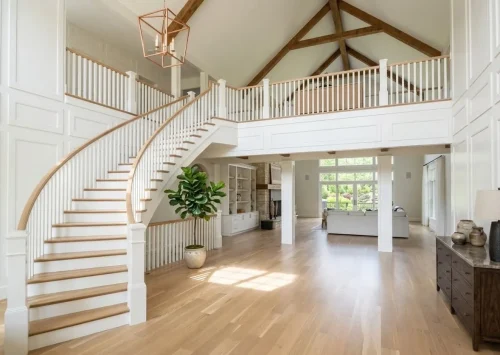 Open foyer with a curved staircase, vaulted ceiling, exposed wood trusses, and an upper-level balcony.