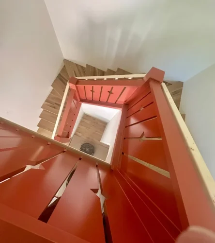 Overhead view of a staircase featuring natural wood steps and a bold red railing with decorative geometric cutouts.