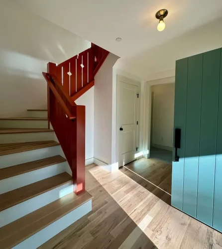 Entryway featuring a bold red staircase railing, natural wood flooring, white walls, and a teal front door.