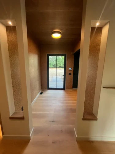 Hallway with wood flooring and ceiling, recessed wall niches, and a glass-paneled exterior door at the far end.