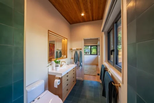 Bathroom with green tile, a wood vanity, a gold-framed mirror, a wood ceiling, and large windows.