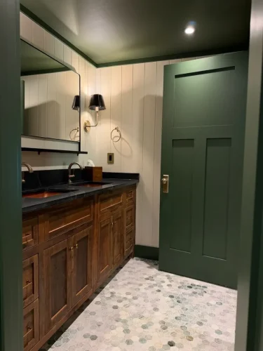 Bathroom with wood vanity, dark countertop, green accents, paneled walls, and hexagonal tile flooring.
