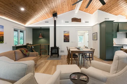 Open living and dining area with wood ceiling, green kitchen cabinets, and wood-burning stove.