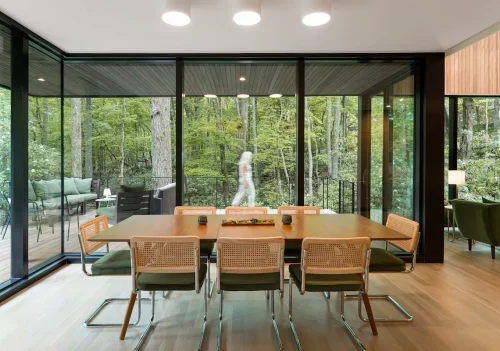 Dining table with eight chairs beside floor-to-ceiling windows.