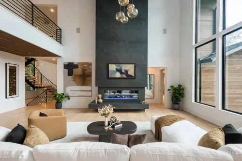Two-story living space with a dramatic slate fireplace, floating hearth, modern chandelier, and large windows filling the room with natural light.