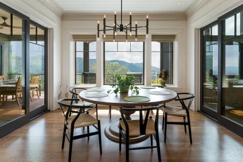 Round dining table with modern black chairs and mountain views through large windows.