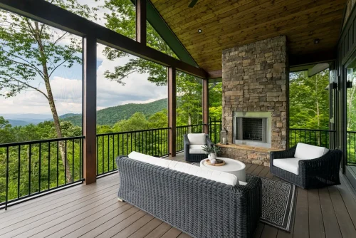 Covered deck with wicker seating, stone fireplace, and expansive mountain views.